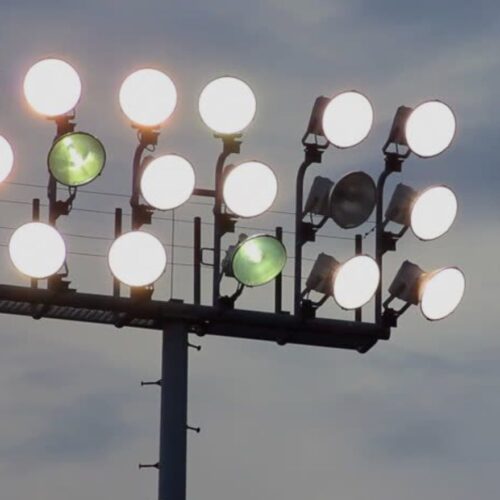 Outdoor stadium lights against a cloudy sky, one light is broken, two lights are dimmed at a different angle